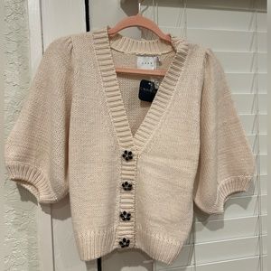 Beige cardigan sweater with black embellished buttons.